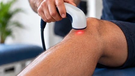 AI-assisted illustration of a therapy applicator held just above the knee with red light directly beneath it.